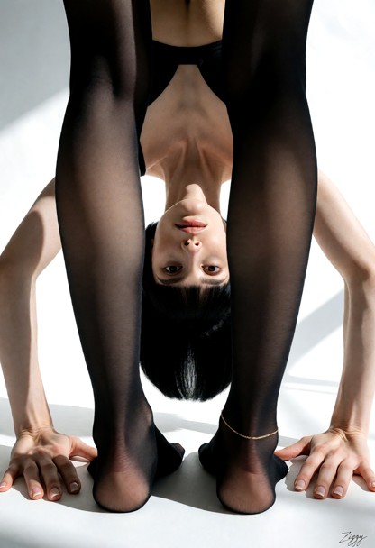 A luxury hosiery campaign photograph in a white sample room. She stands with her feet apart and folds forward from th…