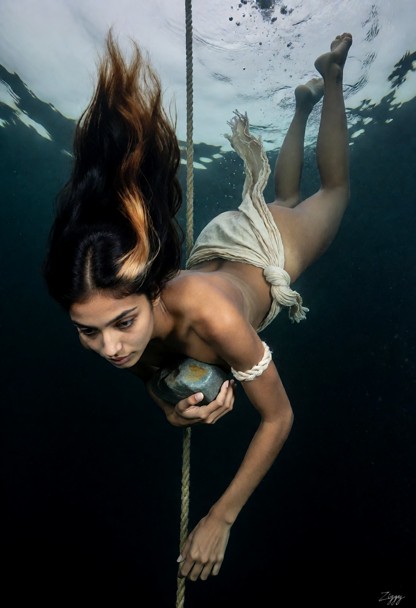 An underwater photograph in deep water, and the water is dark blue-green going to solid black at the bottom of the fr…