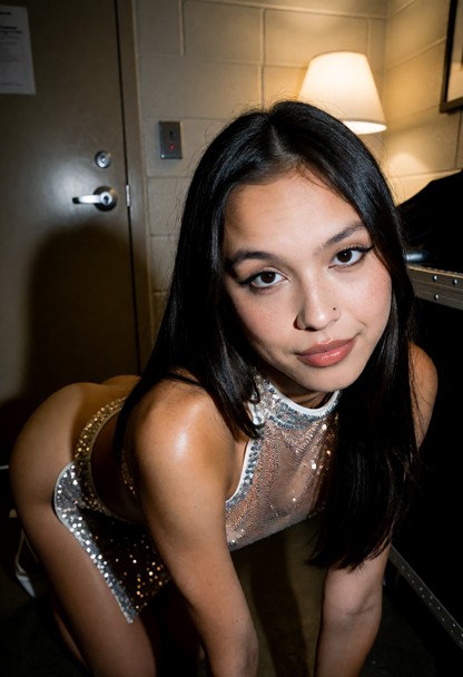 Location: dim, private backstage room behind a heavy door, where soft, warm light from a single lamp creates long sha…