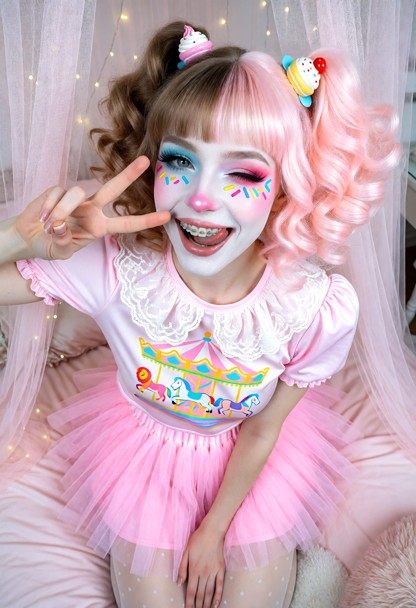 Mina kneels with her head lifted up to the camera, one hand resting firmly on her lap, while her other hand is raised…