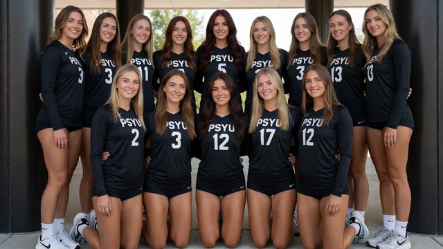 A full-body shot of a university womens volleyball team posing together for a group portrait. The team consists of tw…