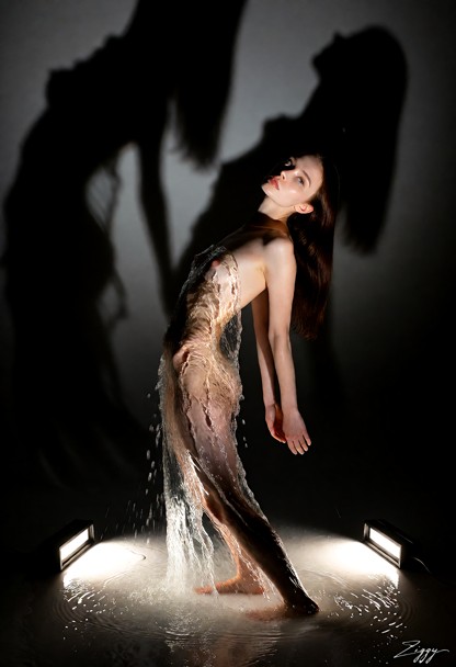 A gown made entirely of clear running water, photographed as a fashion campaign picture in a tall black room lit only…